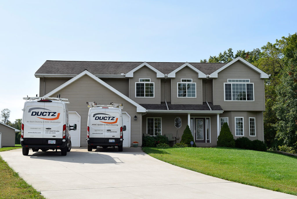 picture of the front of a house with DUCTZ air duct cleaning franchise vans in driveway